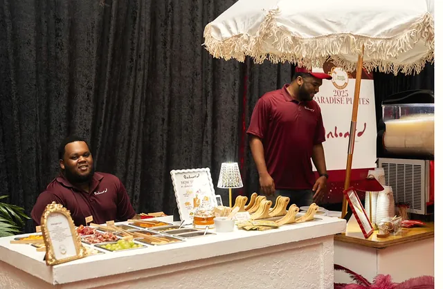 Two Onboard attendants at the charcuterie cart under its fringed parasol