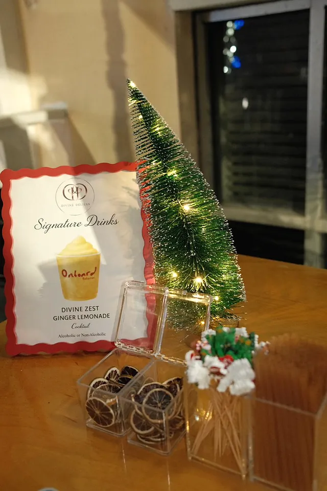 A holiday signature drinks menu beside a small lit Christmas tree